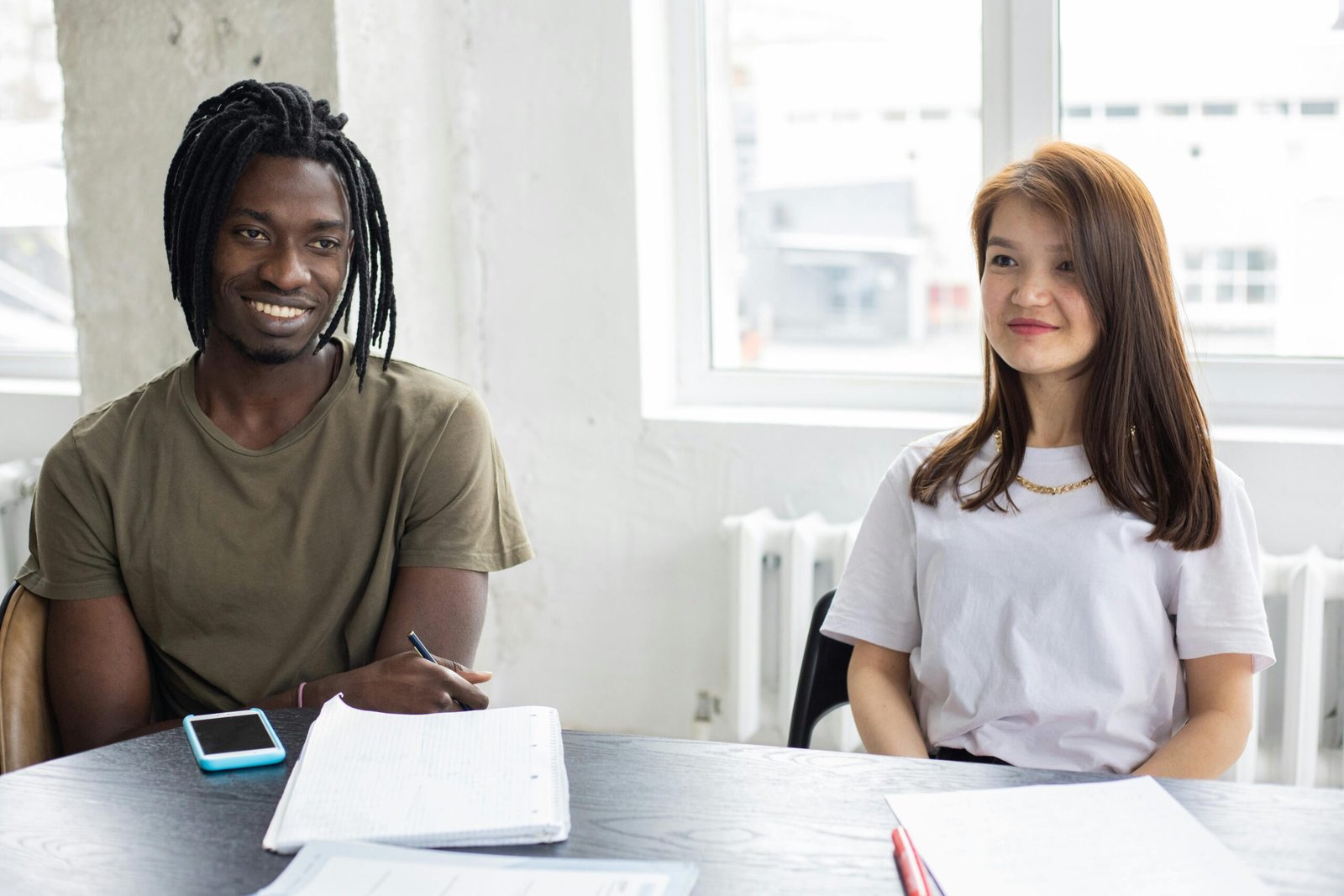 Two diverse college students engaged in a cheerful study session indoors, sharing ideas and knowledge.