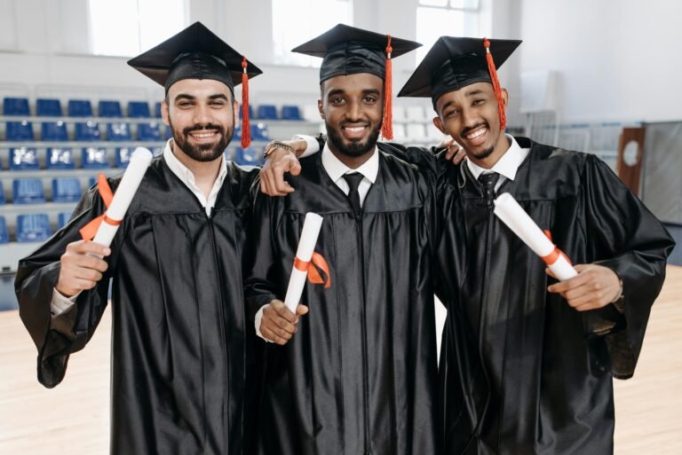 Three graduates in gowns celebrating success with diplomas indoors.
